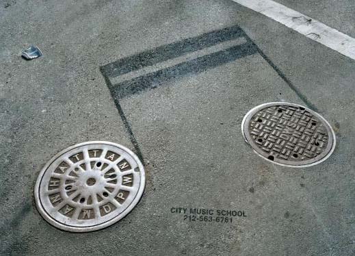 While these manhole covers in front of the Music School in New York City are nondescript on their own, the artwork tying the two together is both creative and playful