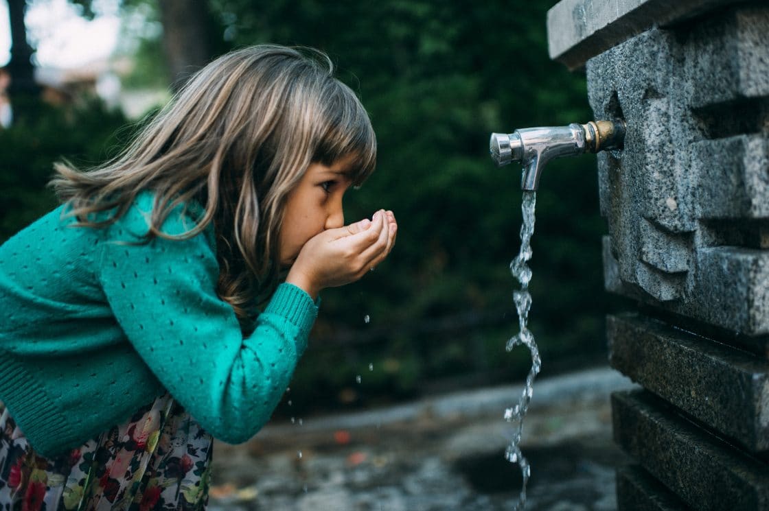 young girl drinking water from outdoor water fountain